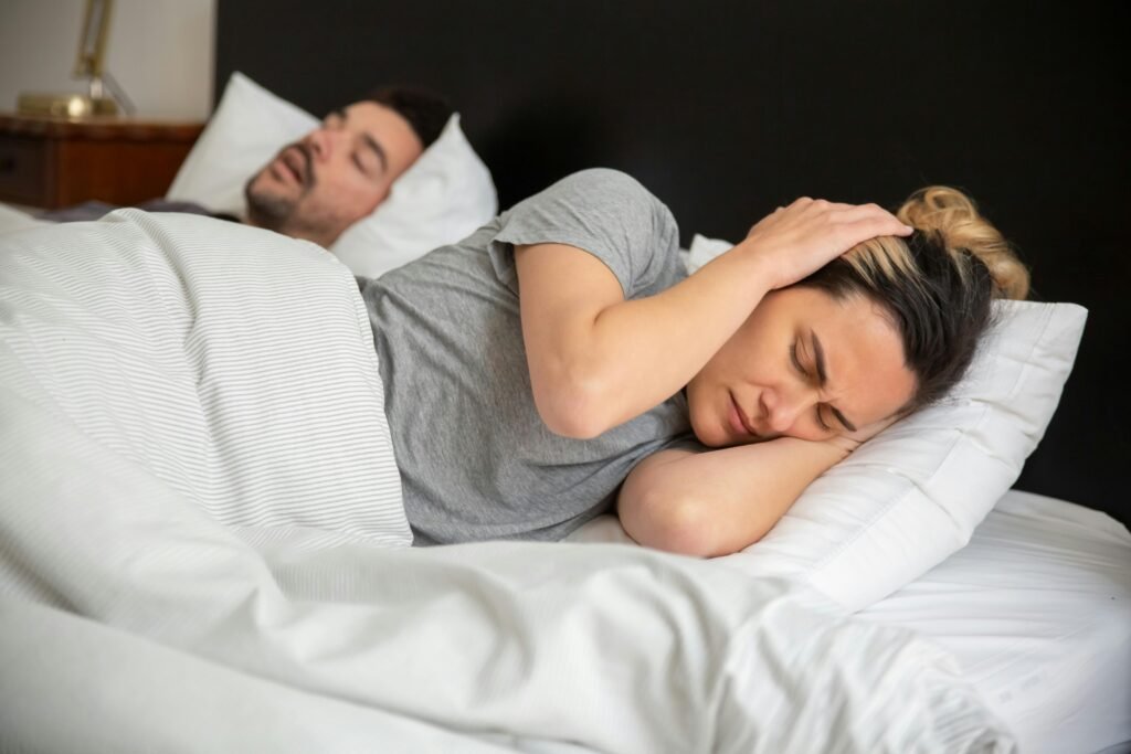 Mujer con tapones en los oídos intentando dormir al lado de su pareja que ronca