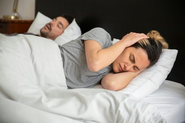 Mujer con tapones en los oídos intentando dormir al lado de su pareja que ronca